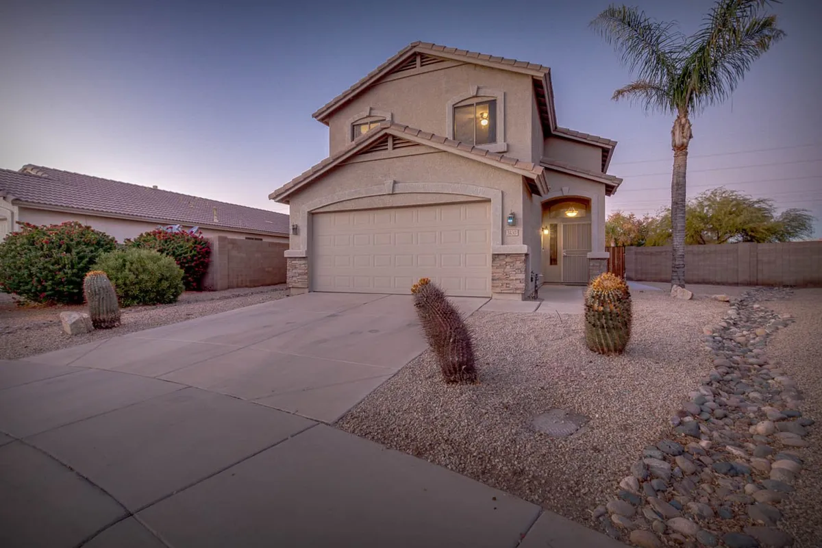 This image showcases the home's welcoming front entrance framed by palms and cacti, with a visible garage door and beautifully maintained landscaping. The inviting exterior hints at a warm Arizona welcome and the home's position in a quiet cul-de-sac.