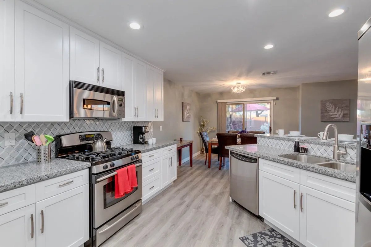 A modern, open kitchen featuring granite countertops, stainless steel appliances, and an adjacent dining area set for a meal. The space is bright and inviting, suggesting a central hub for both daily living and entertaining. The view hints at a functional layout designed for cooking, sharing meals, and feeling at home—ideal for longer stays.