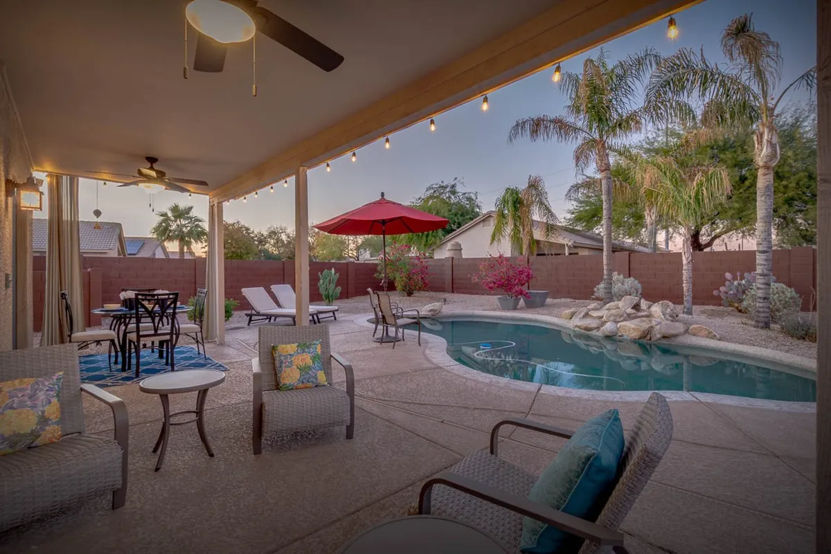A tranquil poolside scene at dusk features shimmering water, comfortable outdoor seating, potted plants, and string lights overhead. The setup is ideal for both daytime relaxation and evening gatherings under the stars.