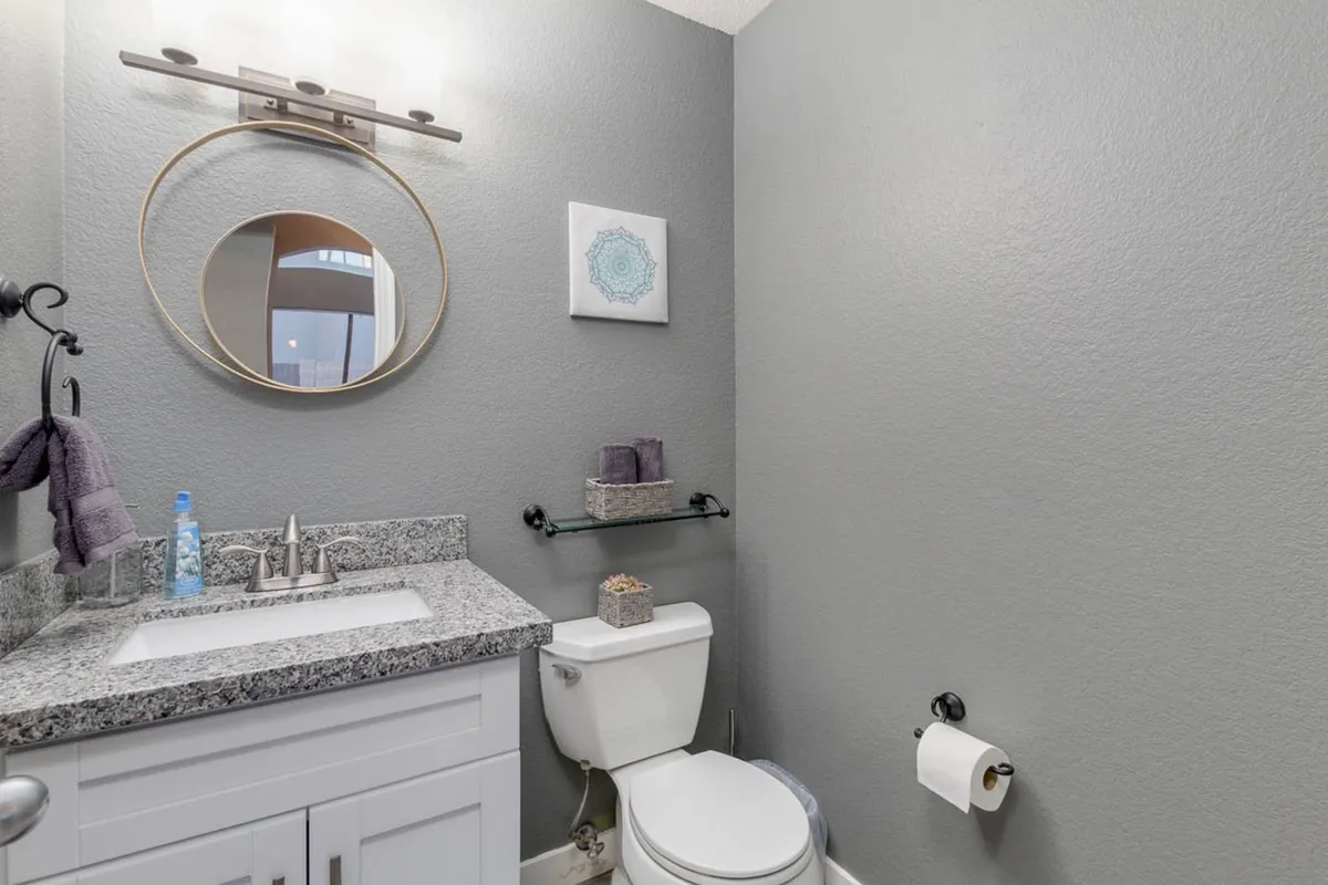 A calm and inviting bathroom scene with a vanity, round mirror, granite countertop, and decorative artwork. The space exudes serenity, making it perfect for morning or evening self-care routines.