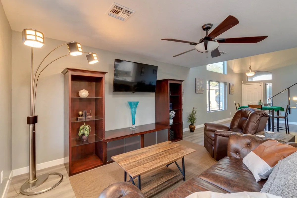 A cozy, inviting living room scene with a leather sofa, wooden coffee table, TV, bookshelf, and decorative accents like a blue vase. The arrangement suggests a space perfect for watching movies, socializing, or playing games together.