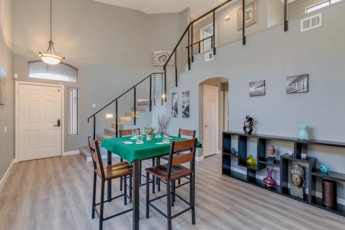 A cozy and inviting dining nook with a green tablecloth, staircase, decorative shelf, and wall art. The setting is ideal for casual meals, game nights, or small group conversations, capturing the essence of togetherness and relaxation.