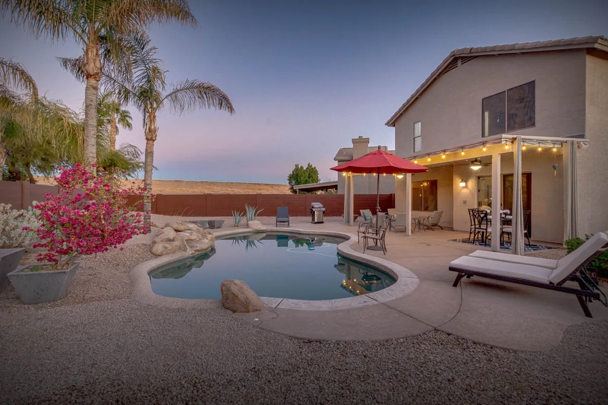 A tranquil backyard scene featuring a sparkling swimming pool, red patio umbrella, comfortable outdoor seating, and flowering plants. The atmosphere is serene and playful, ideal for families looking to relax or have fun after exploring nearby attractions.