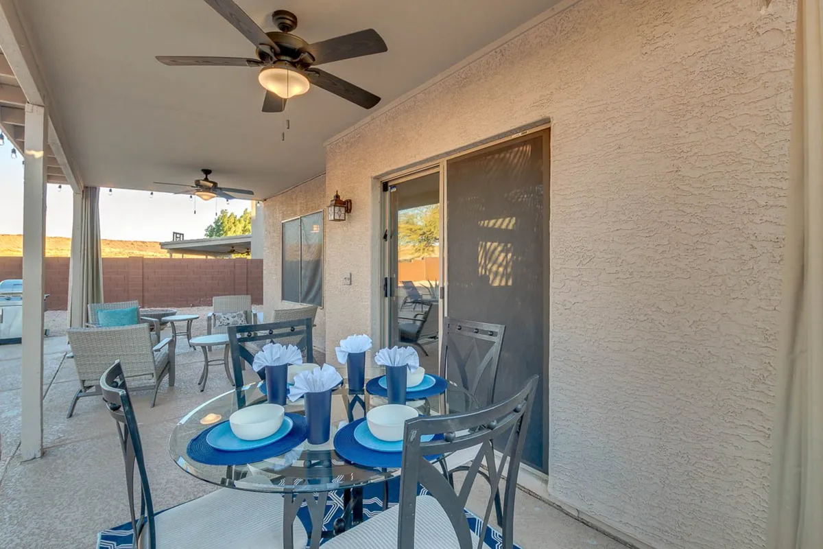 A covered outdoor dining area featuring a long, decorated table set for a group, with comfortable seating and a ceiling fan overhead. The space is inviting for social gatherings, meals, and relaxation, while also allowing guests to enjoy the outdoors in comfort.