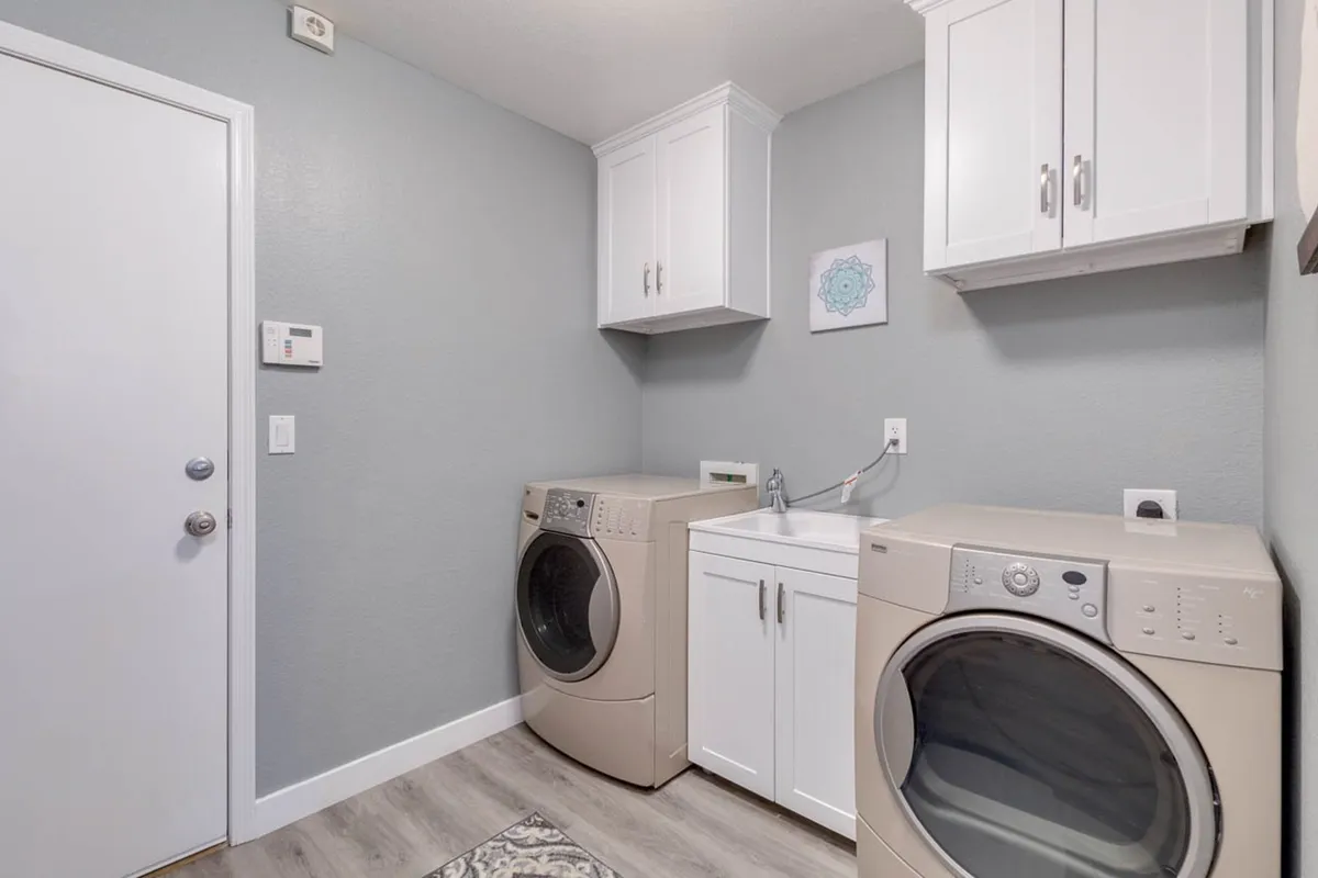 A well-organized laundry room with a washer and dryer, built-in storage cabinets, a sink for convenience, and decorative wall art that adds a homely touch. The space looks clean, practical, and ready for extended use—ideal for guests planning longer stays.