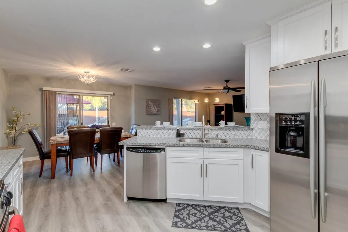 A bright, airy kitchen with a spacious island, dining table, and abundant natural light streaming in from large windows. The layout encourages both meal prep and comfortable dining, with plenty of room for guests or family to gather.