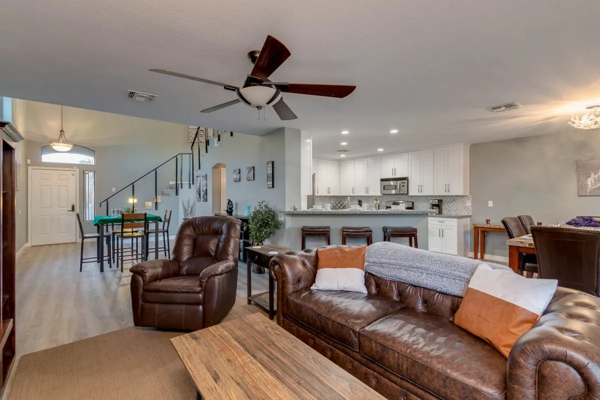 This open-concept interior features a leather sofa, dining table, kitchen island, and a staircase, creating a seamless flow between spaces. The setting is bright and comfortable, designed for both social gatherings and game nights.