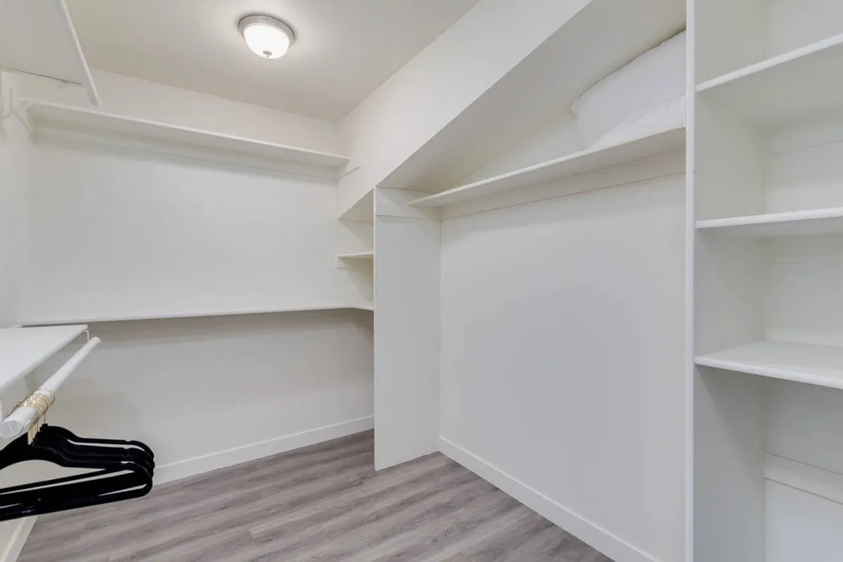 A spacious walk-in closet featuring shelves, hangers, and a soft overhead light. The minimalistic design makes it easy to visualize organizing clothing and personal items, promoting a sense of home and long-term comfort.